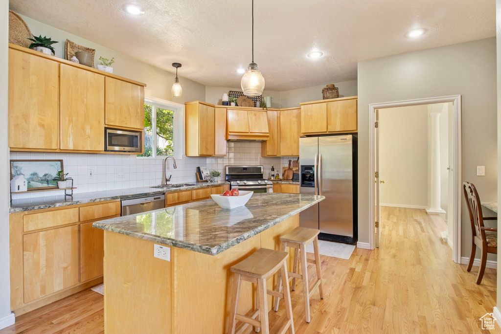 Kitchen featuring stainless steel appliances, a sink, decorative backsplash, light wood finished floors, and a breakfast bar