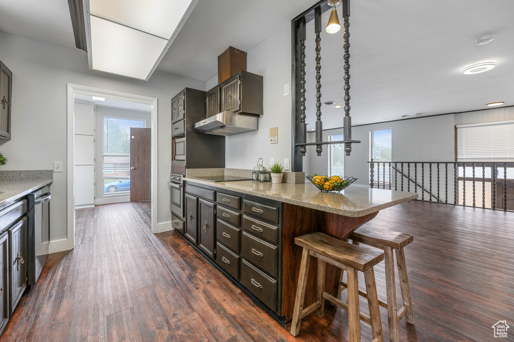 Kitchen featuring a kitchen breakfast bar, dark wood-style flooring, light stone counters, a peninsula, and stainless steel appliances