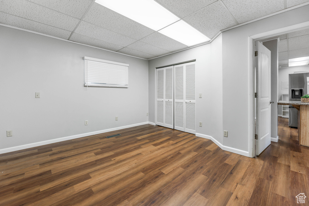 Unfurnished bedroom with stainless steel refrigerator with ice dispenser, a paneled ceiling, baseboards, and dark wood-style floors