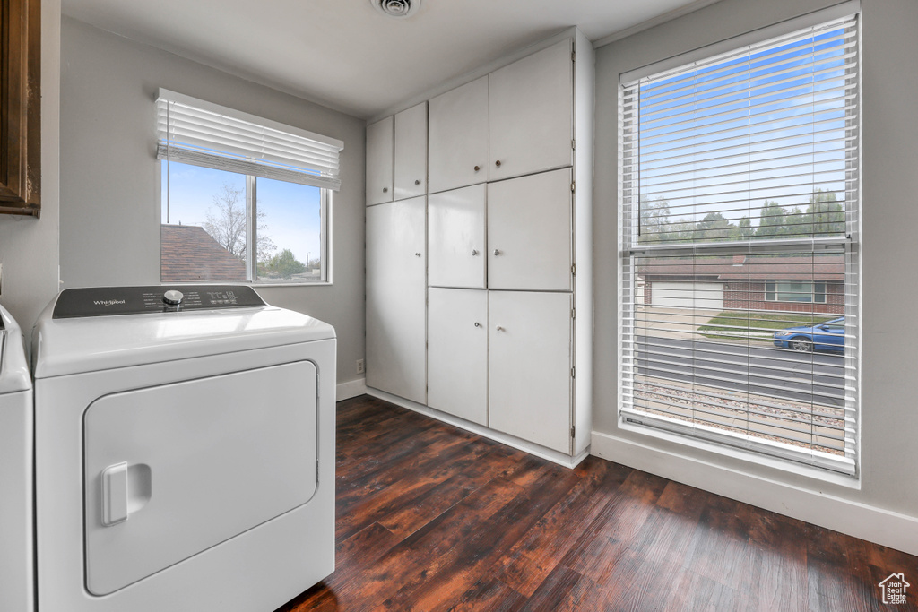 Laundry area featuring dark wood-style flooring, visible vents, cabinet space, baseboards, and washer and dryer