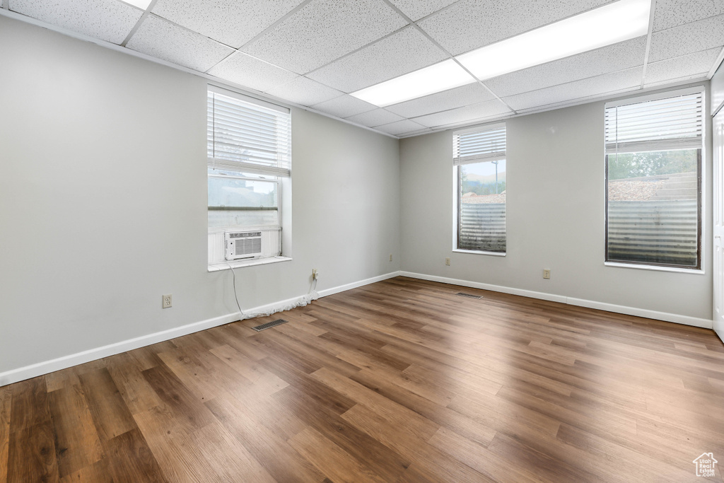Empty room with wood finished floors, baseboards, a drop ceiling, and cooling unit