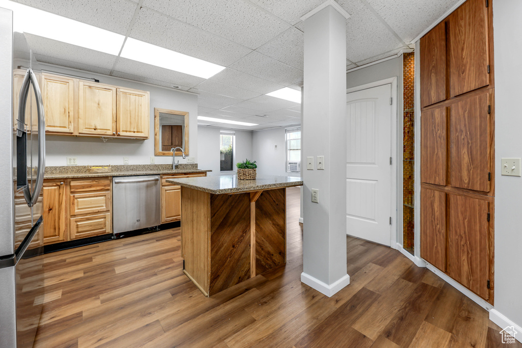 Kitchen featuring light stone countertops, appliances with stainless steel finishes, a paneled ceiling, light wood-style flooring, and a center island