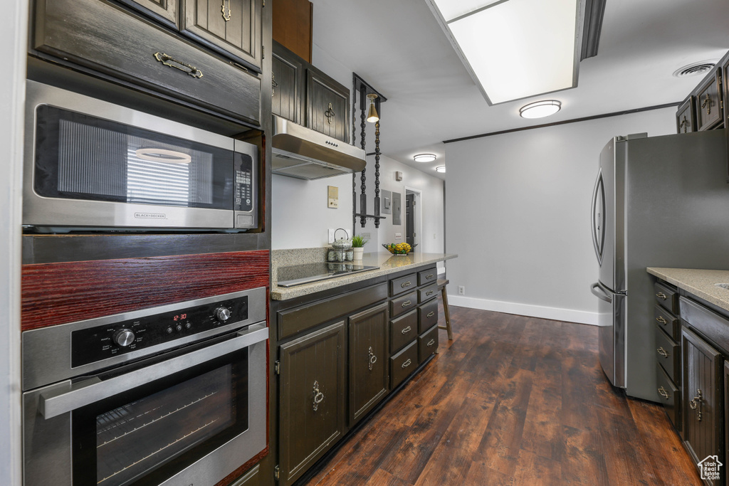 Kitchen featuring light stone countertops, baseboards, dark wood-type flooring, under cabinet range hood, and stainless steel appliances