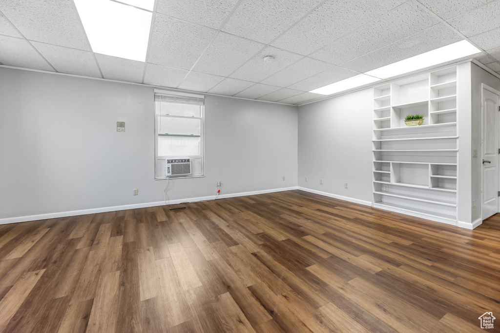 Unfurnished room with cooling unit, baseboards, a drop ceiling, and dark wood-type flooring