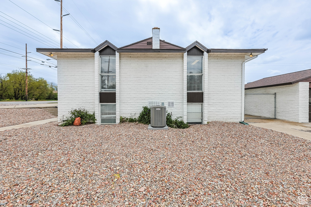 Back of house with a chimney, cooling unit, and brick siding