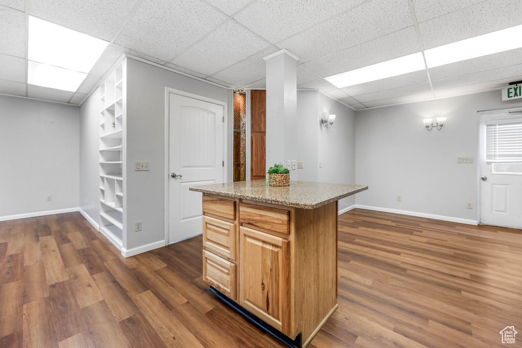 Kitchen with dark wood-style flooring, a kitchen island, light stone countertops, baseboards, and a paneled ceiling