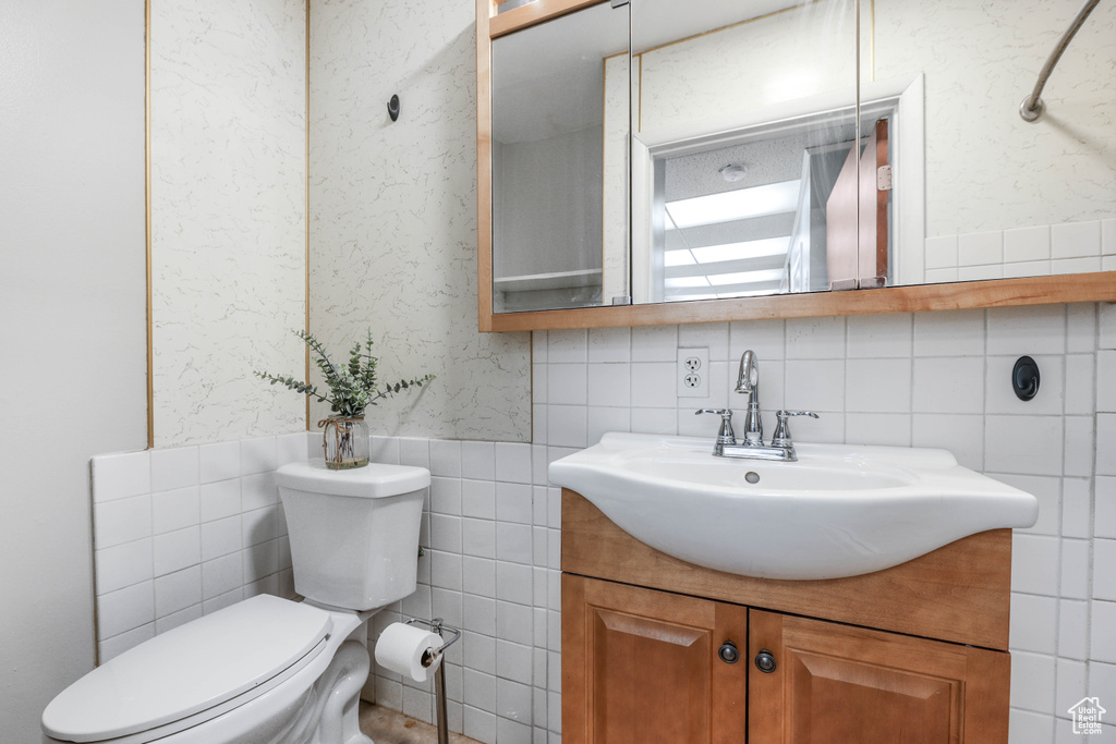 Bathroom with tile walls, a wainscoted wall, vanity, and toilet