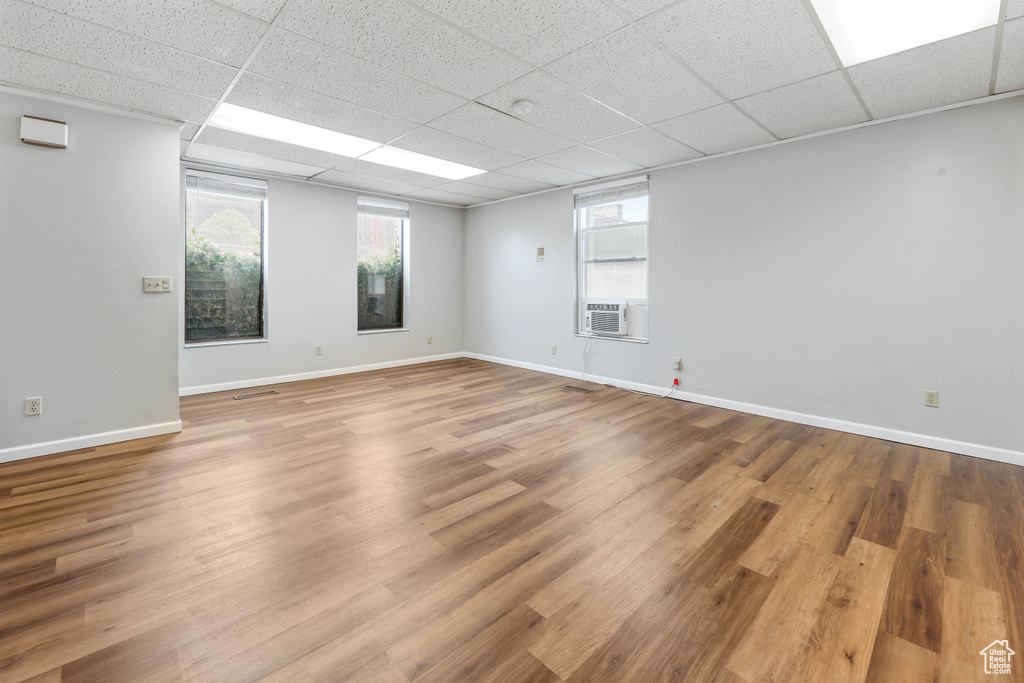 Empty room with cooling unit, a drop ceiling, a healthy amount of sunlight, and wood finished floors