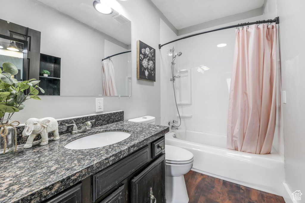 Full bath with vanity, shower / bath combo with shower curtain, toilet, and wood finished floors