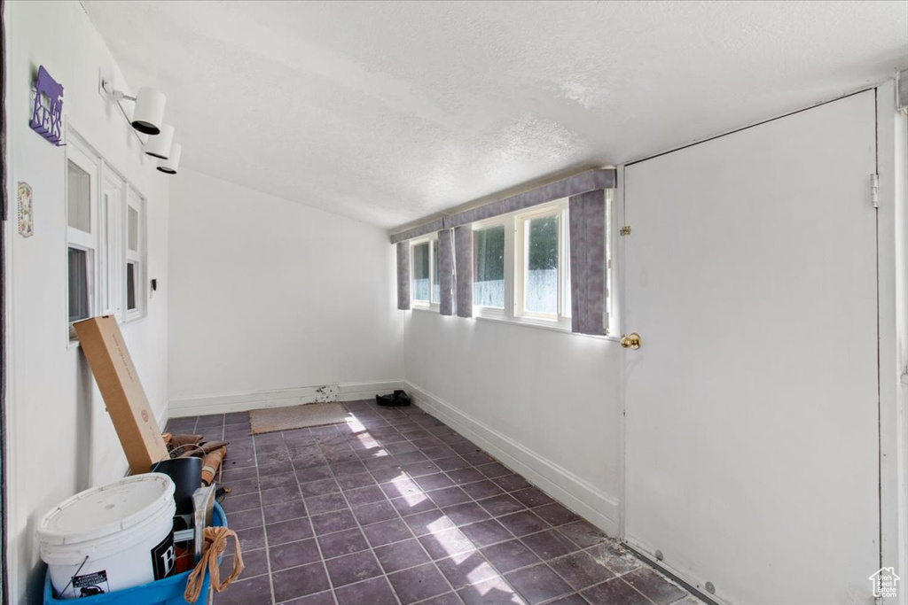 Empty room with a textured ceiling, dark tile patterned flooring, and baseboards
