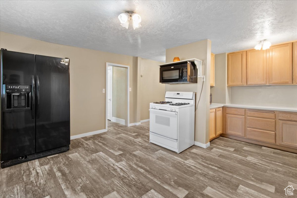 Kitchen with black appliances, light brown cabinets, light wood-type flooring, light countertops, and a textured ceiling