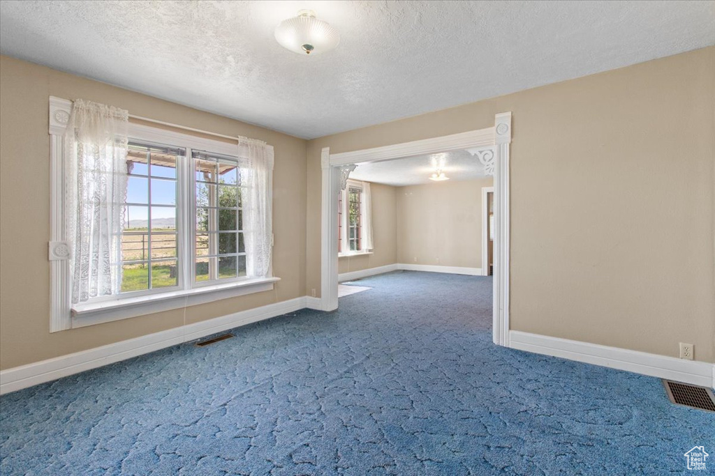 Carpeted spare room featuring baseboards, a textured ceiling, and a chandelier