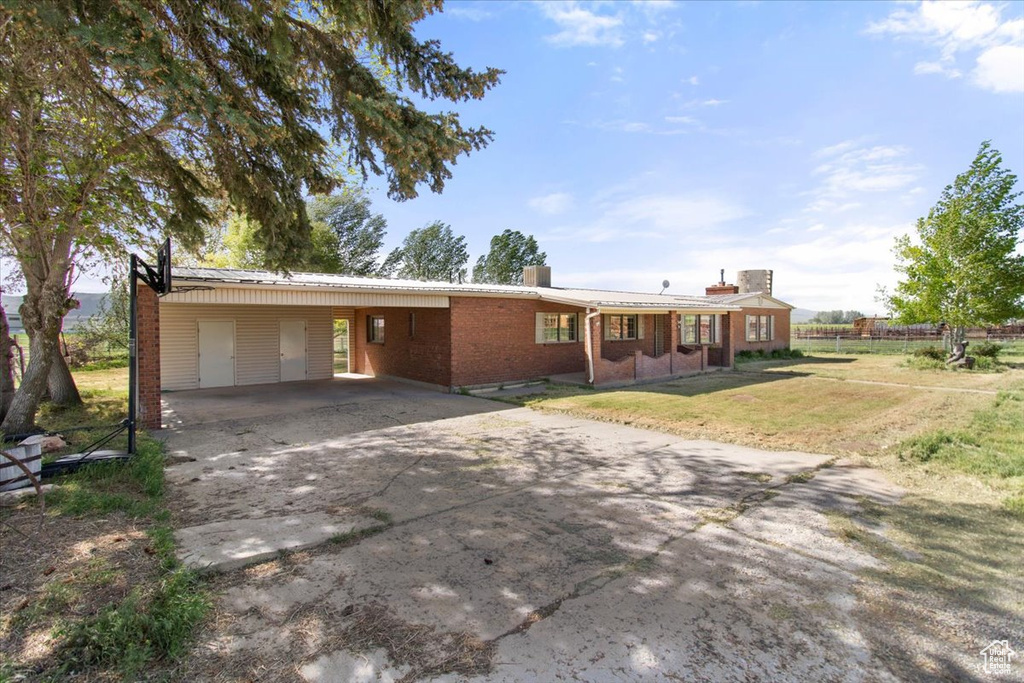 Single story home featuring a chimney, driveway, a carport, brick siding, and metal roof