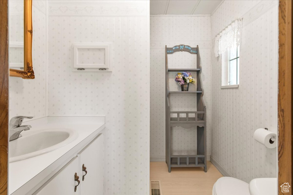 Half bath with wood finished floors, toilet, vanity, and crown molding