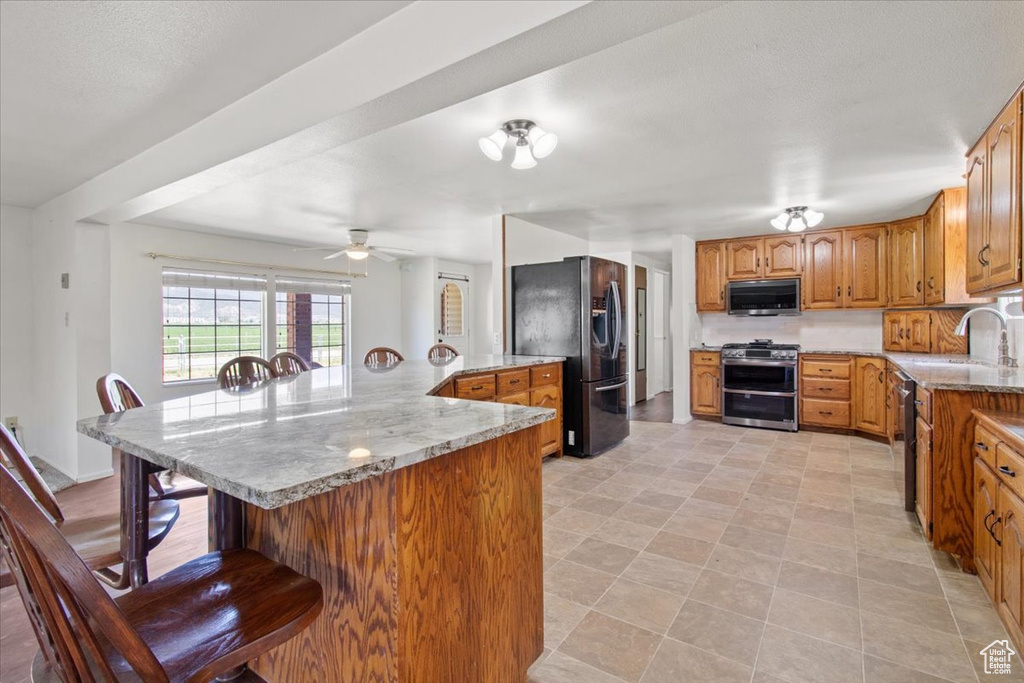 Kitchen featuring appliances with stainless steel finishes, a sink, a kitchen breakfast bar, a ceiling fan, and brown cabinets