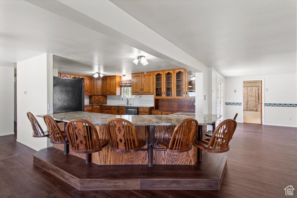 Kitchen featuring freestanding refrigerator, brown cabinets, wallpapered walls, a peninsula, and stainless steel dishwasher
