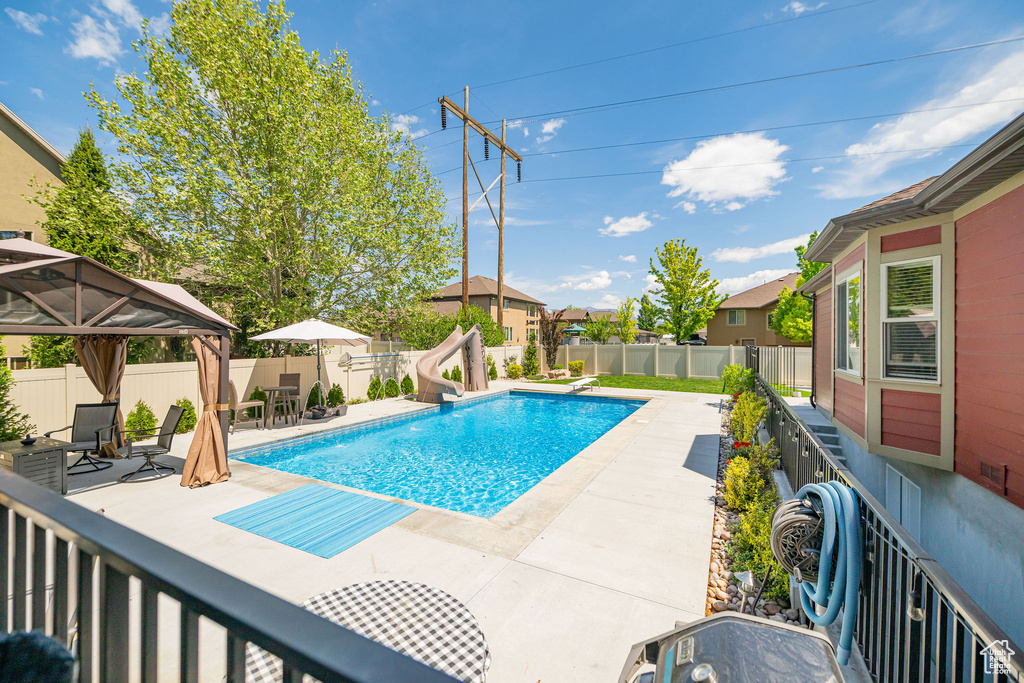 View of swimming pool with a water slide, a patio, a fenced backyard, a gazebo, and a diving board