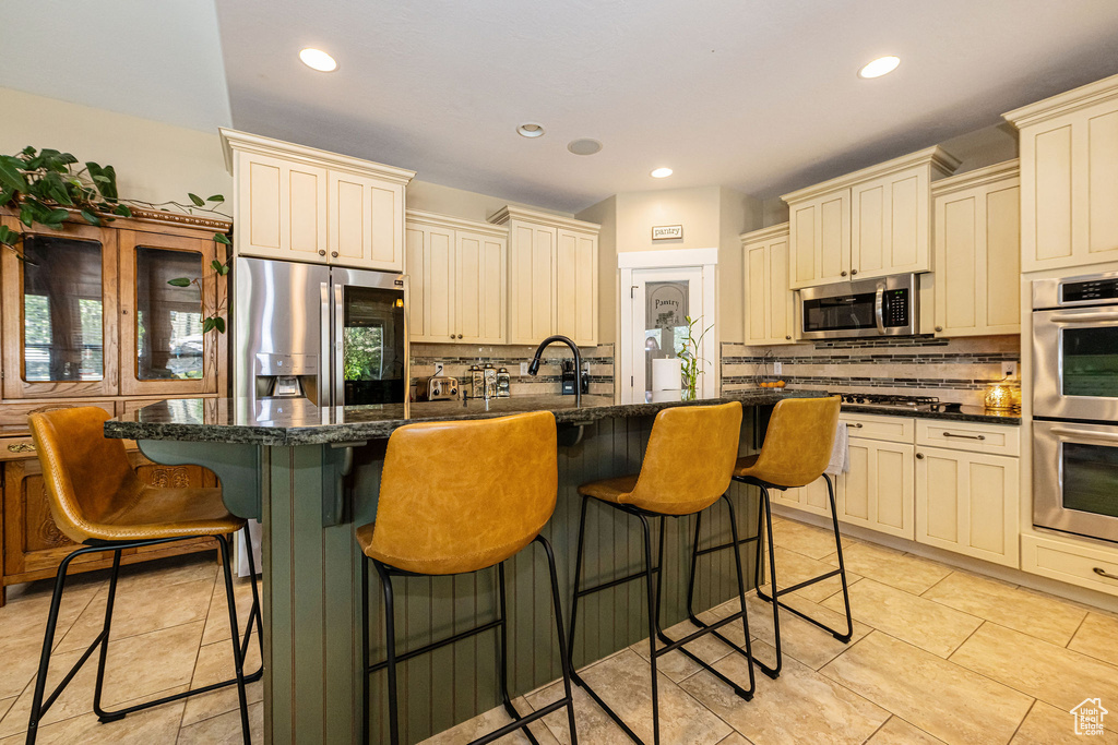 Kitchen with stainless steel appliances, cream cabinets, tasteful backsplash, recessed lighting, and a kitchen island with sink