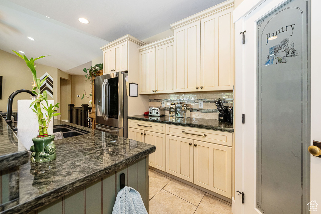 Kitchen with stainless steel fridge, cream cabinets, decorative backsplash, a sink, and light tile patterned floors