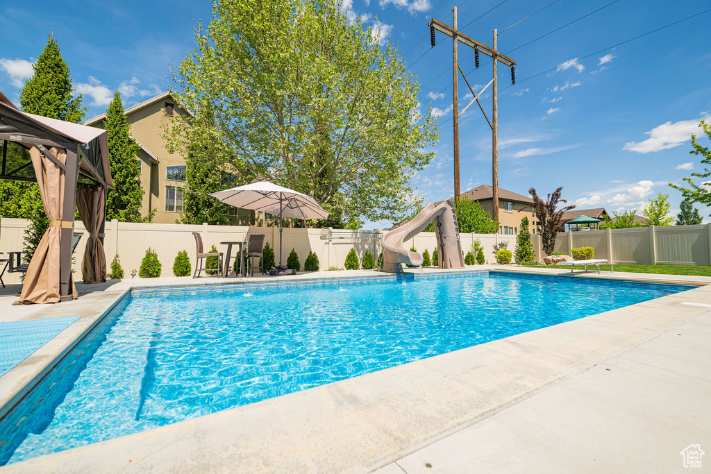 View of pool with a water slide, a fenced backyard, a gazebo, and a patio area