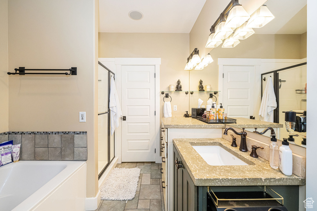 Bathroom featuring stone tile flooring, a shower stall, a garden tub, vanity, and a chandelier