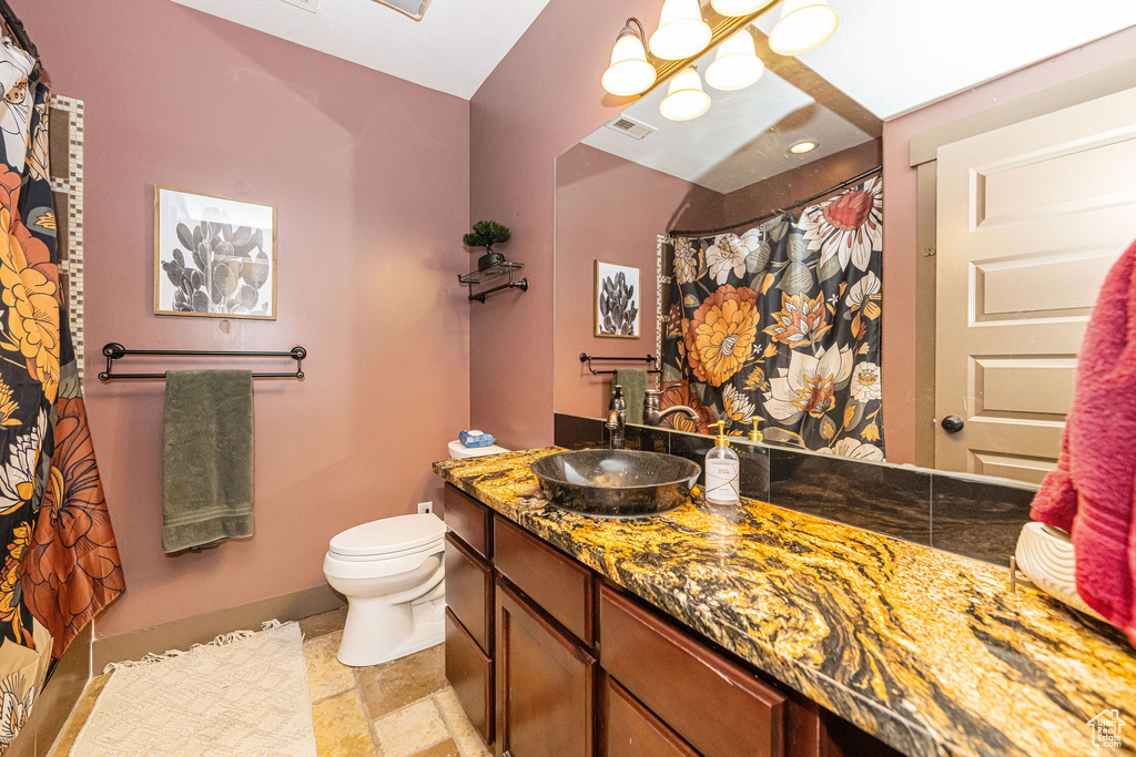 Bathroom with toilet, vanity, stone finish flooring, a chandelier, and baseboards