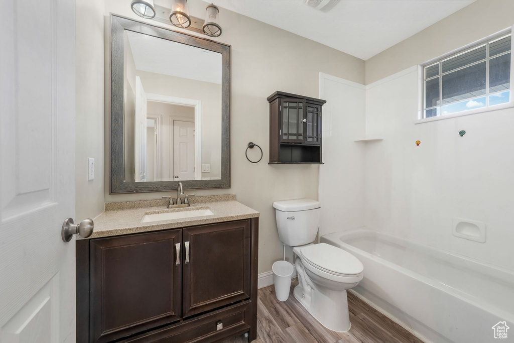 Bathroom featuring toilet, vanity, wood finished floors, shower / bath combination, and baseboards