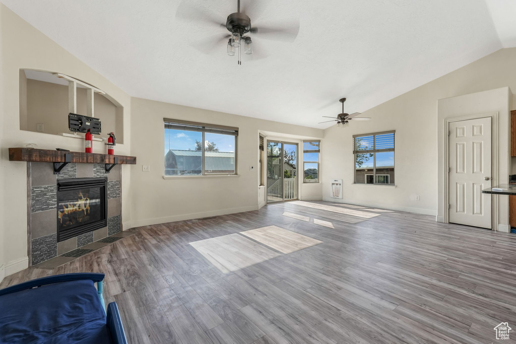 Unfurnished living room featuring a ceiling fan, a fireplace, lofted ceiling, wood finished floors, and plenty of natural light