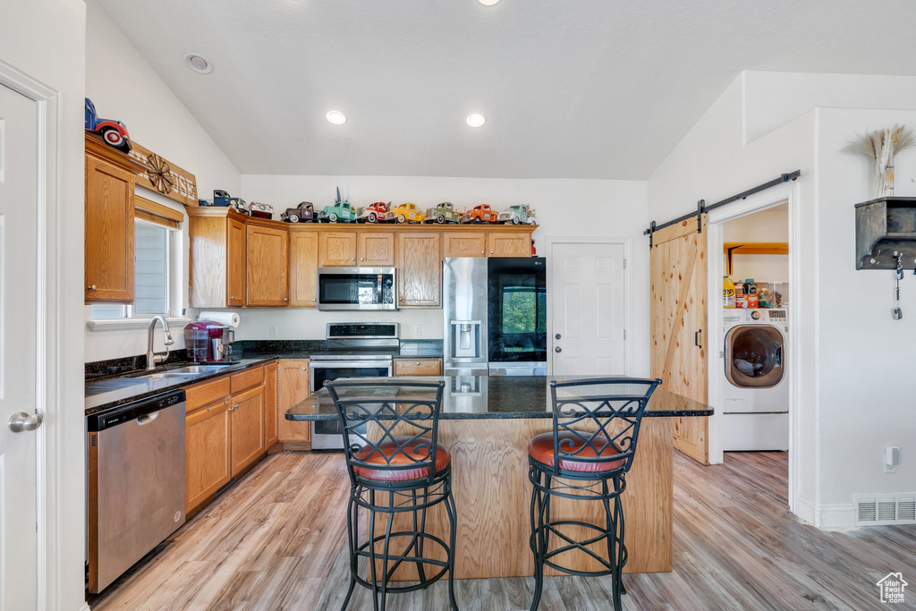 Kitchen featuring appliances with stainless steel finishes, a sink, washer / dryer, a barn door, and light wood-style flooring