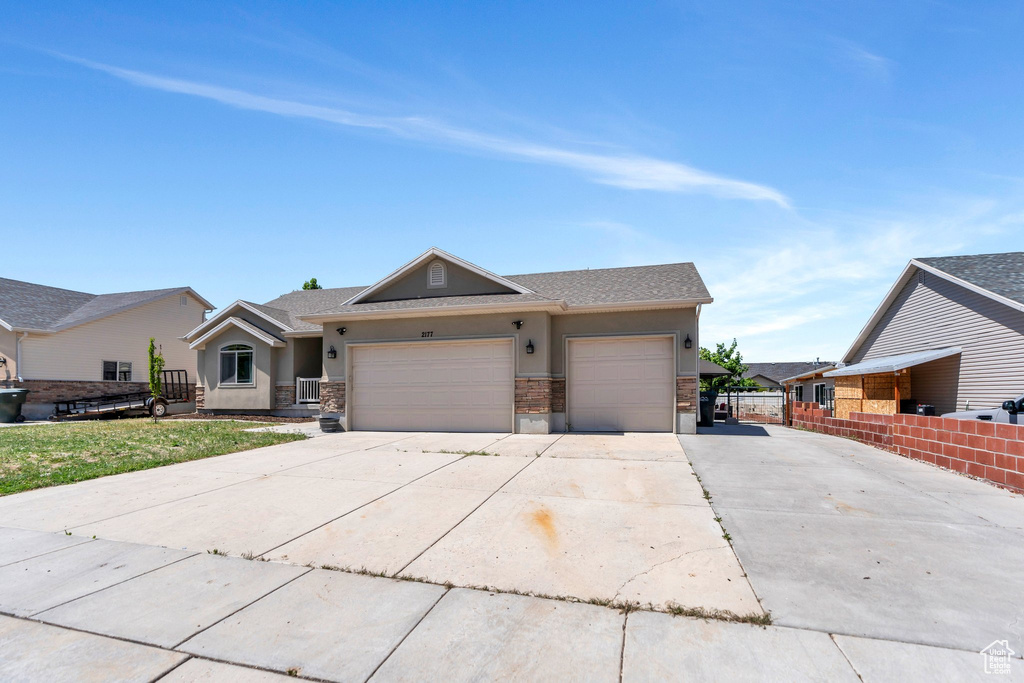 View of front facade with stucco siding, concrete driveway, an attached garage, fence, and stone siding