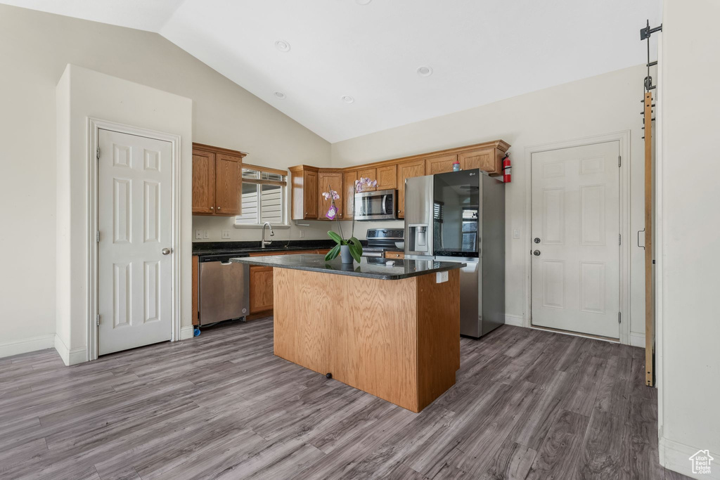 Kitchen featuring stainless steel appliances, a center island, wood finished floors, a sink, and dark countertops