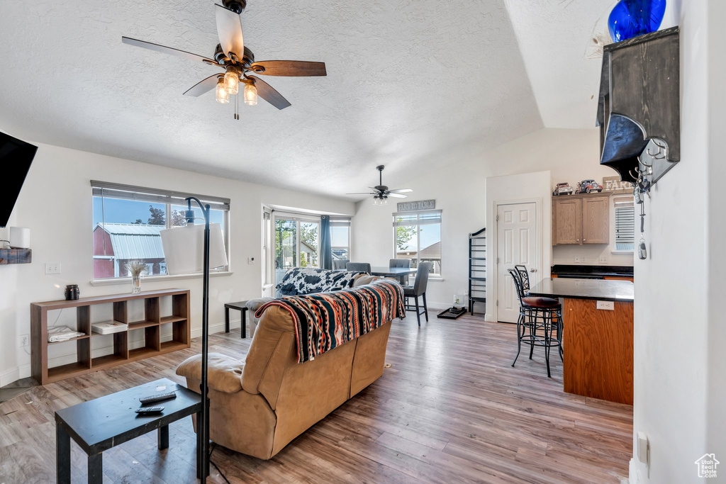 Living room with a ceiling fan, lofted ceiling, a textured ceiling, light wood finished floors, and baseboards