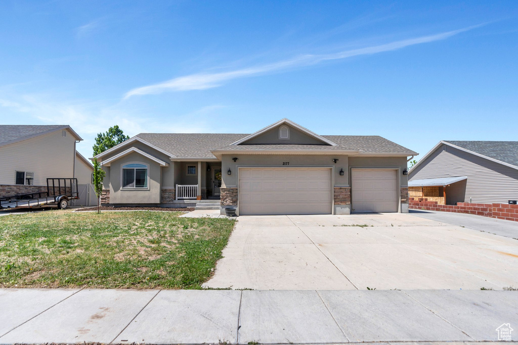 Single story home featuring a garage, concrete driveway, stucco siding, a front lawn, and stone siding