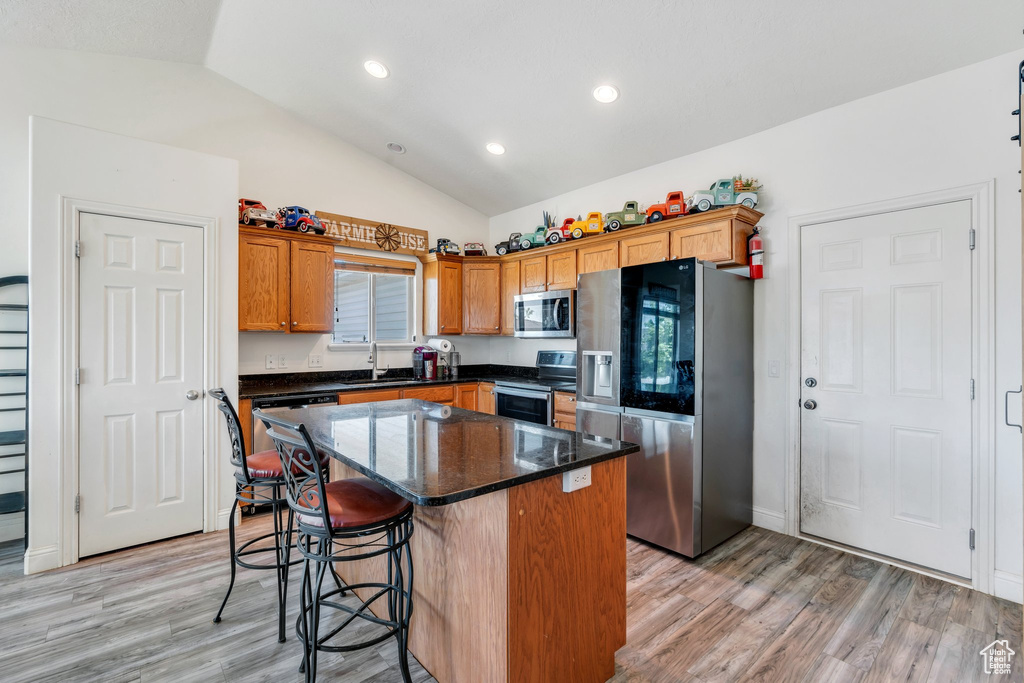 Kitchen with stainless steel appliances, vaulted ceiling, light wood-type flooring, a kitchen bar, and a kitchen island