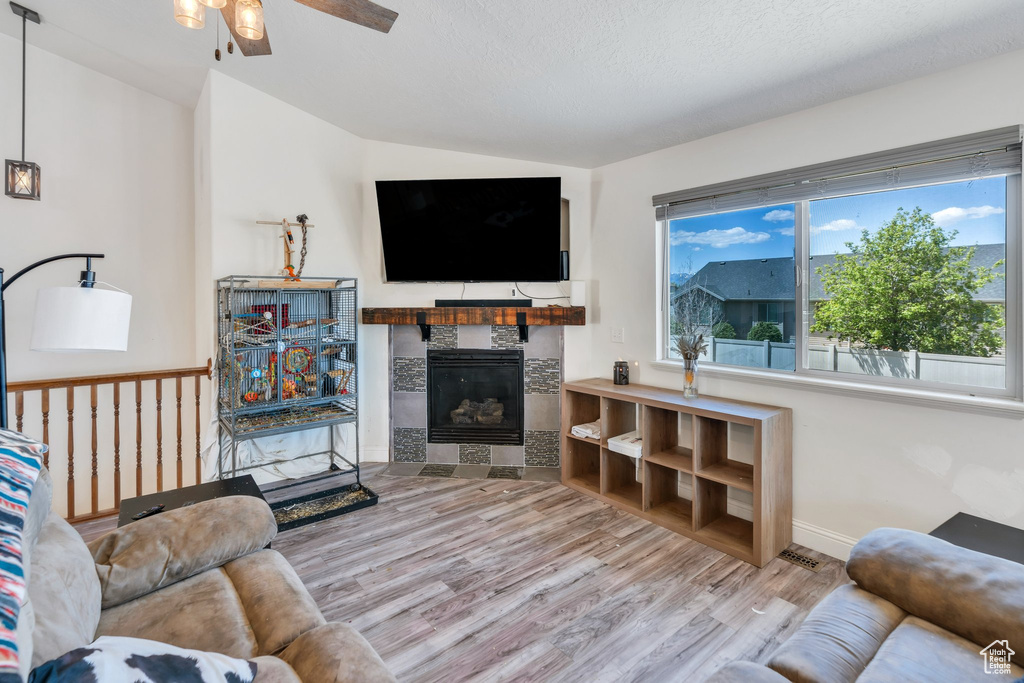 Living area with a ceiling fan, wood finished floors, a tile fireplace, vaulted ceiling, and baseboards