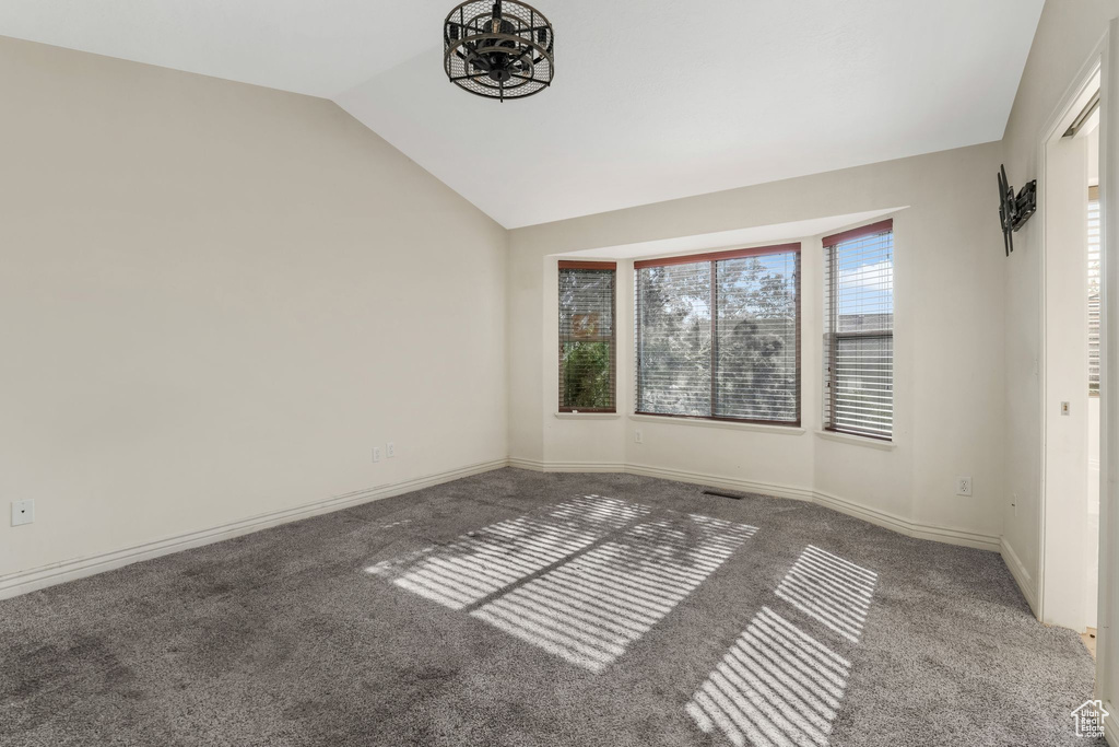Carpeted spare room featuring vaulted ceiling, baseboards, and a chandelier