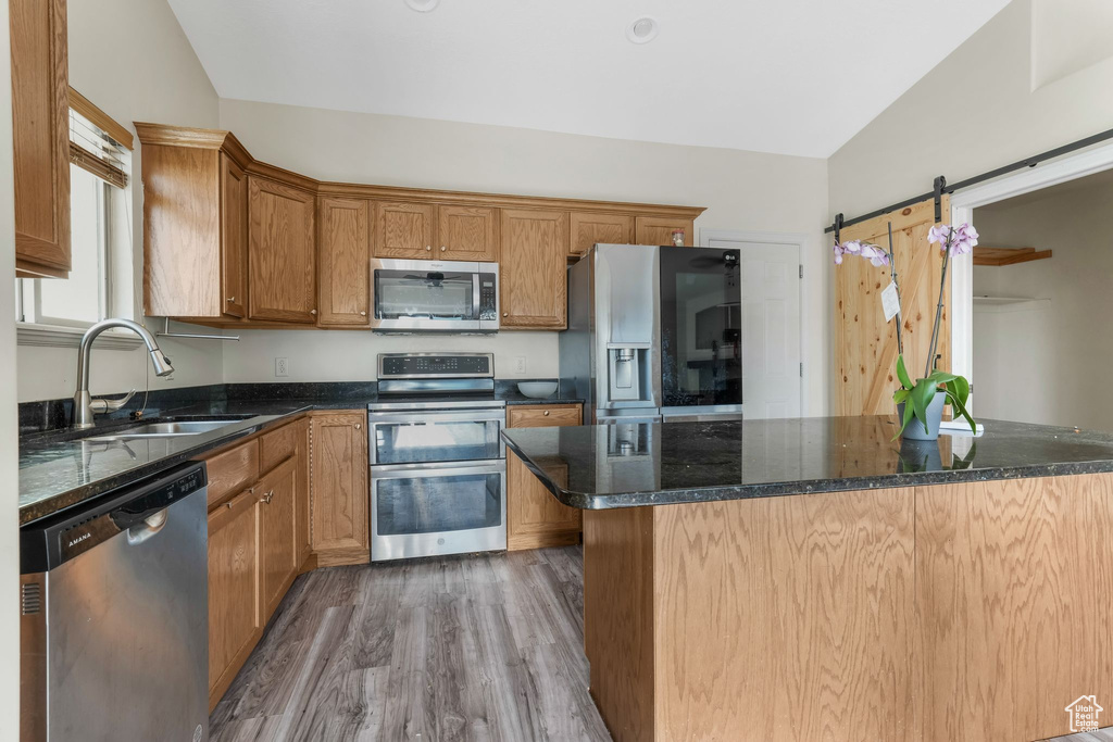 Kitchen featuring appliances with stainless steel finishes, a sink, wood finished floors, dark stone countertops, and brown cabinetry