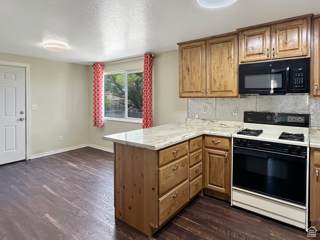Kitchen with gas stove, black microwave, a peninsula, dark wood-style floors, and decorative backsplash