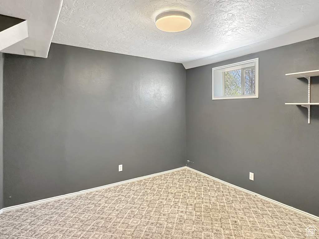 Empty room featuring a textured ceiling, carpet, and baseboards
