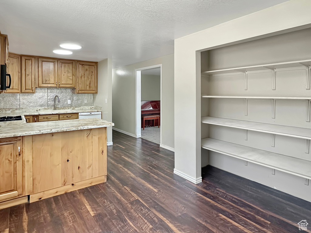 Kitchen with black microwave, light stone countertops, dark wood-style flooring, a sink, and baseboards
