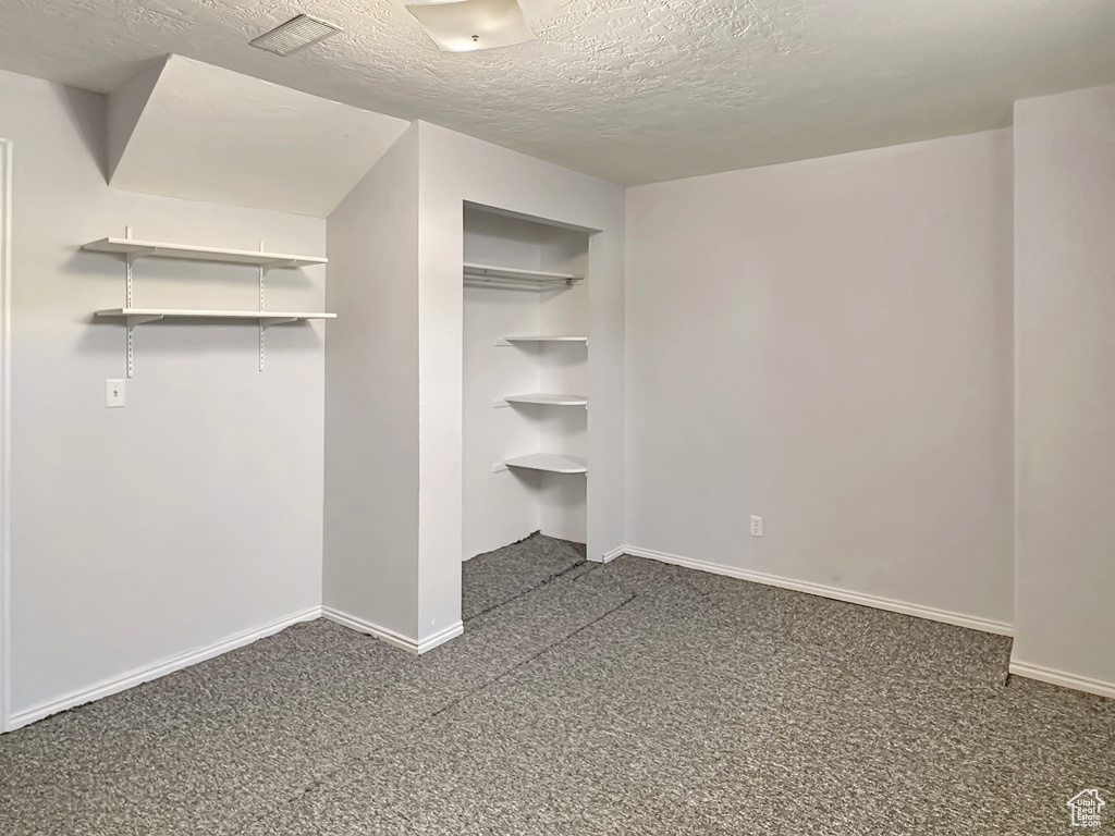 Unfurnished bedroom with a textured ceiling, dark colored carpet, baseboards, and a closet
