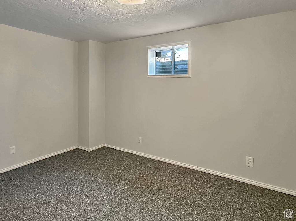 Empty room with dark carpet, baseboards, and a textured ceiling