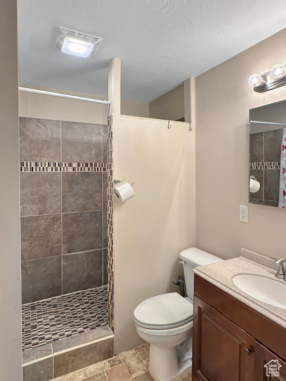 Bathroom featuring a tile shower, toilet, and vanity