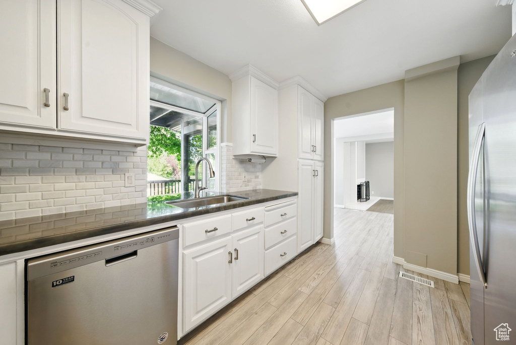 Kitchen with stainless steel appliances, a sink, white cabinets, light wood-style flooring, and decorative backsplash