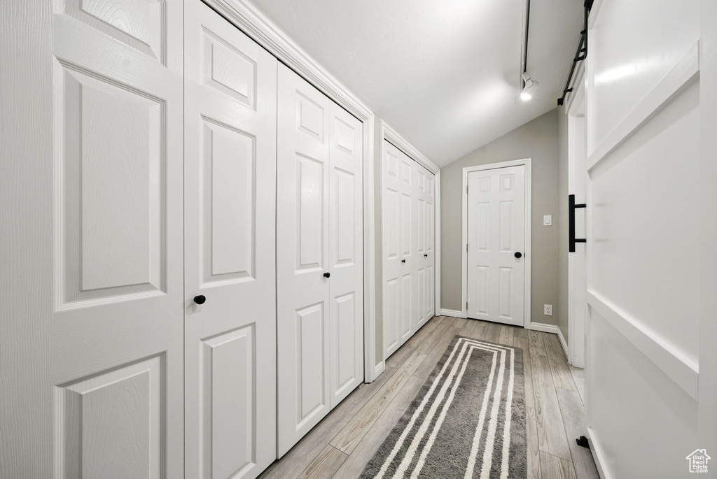 Hallway featuring vaulted ceiling, light wood-style floors, and baseboards