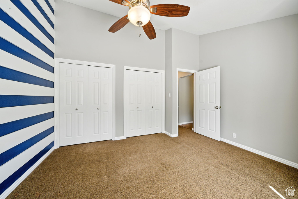 Unfurnished bedroom featuring carpet, two closets, baseboards, a high ceiling, and a ceiling fan
