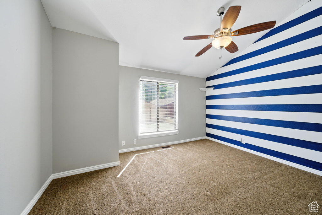 Empty room featuring ceiling fan, carpet floors, vaulted ceiling, and baseboards