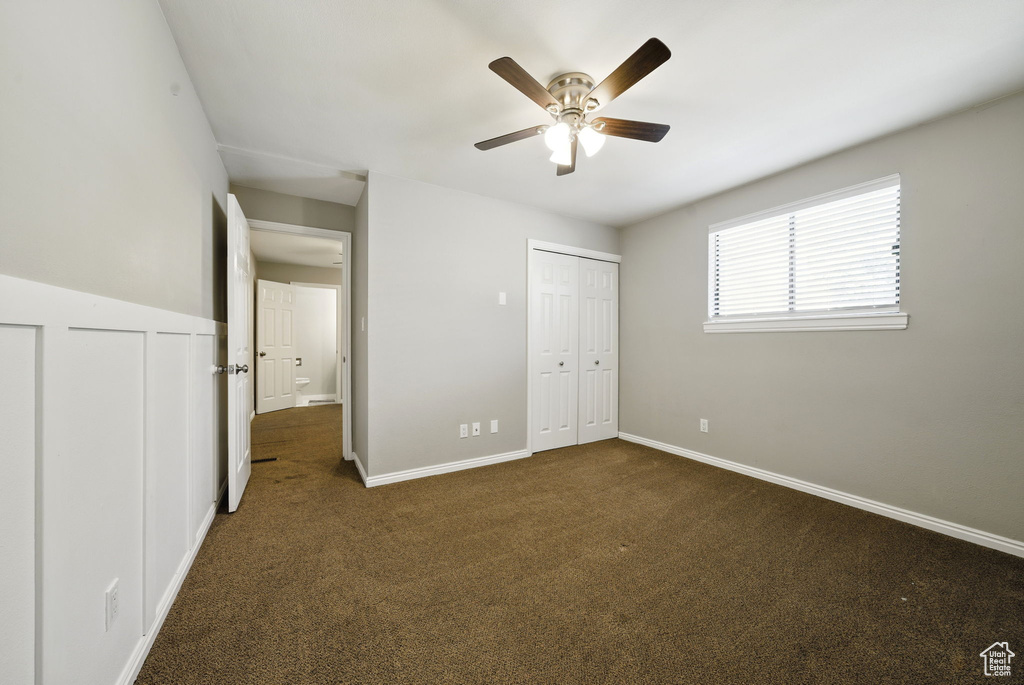 Unfurnished bedroom with dark carpet, baseboards, and a ceiling fan