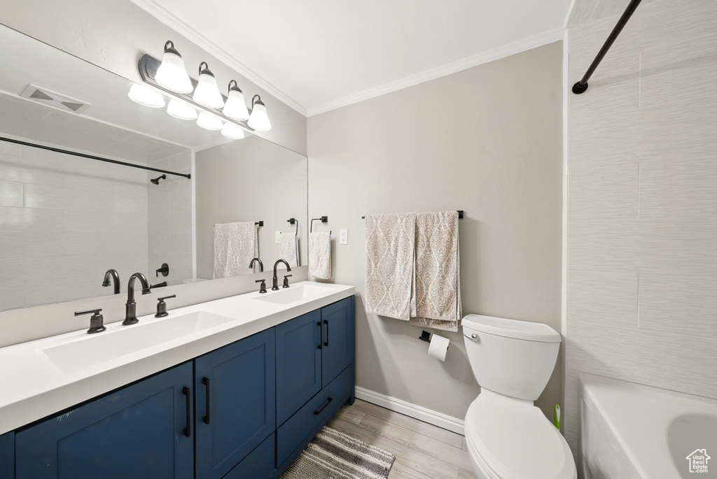 Bathroom featuring toilet, crown molding, baseboards, wood finished floors, and double vanity