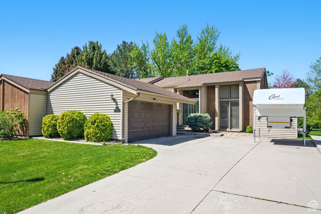 View of front facade featuring a garage, concrete driveway, a front yard, and a shingled roof